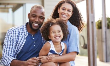 Image Text: Young black family embracing outdoors and smiling at camera